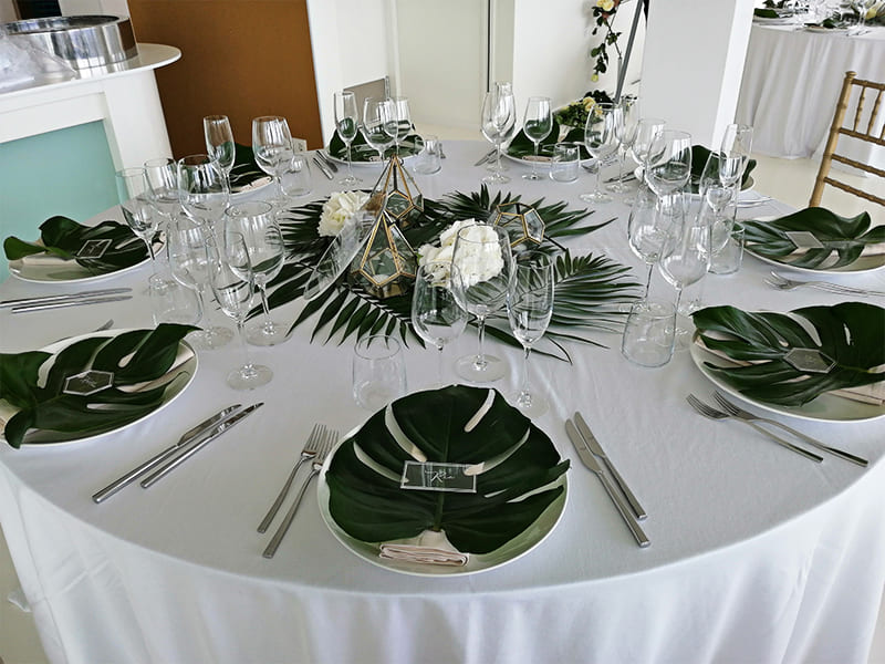 Mesa redonda con hojas de palmera, vasos de vino y decoración dorada