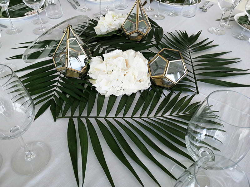 Hojas de palmera en una mesa blanca con caquitas de velas doradas
