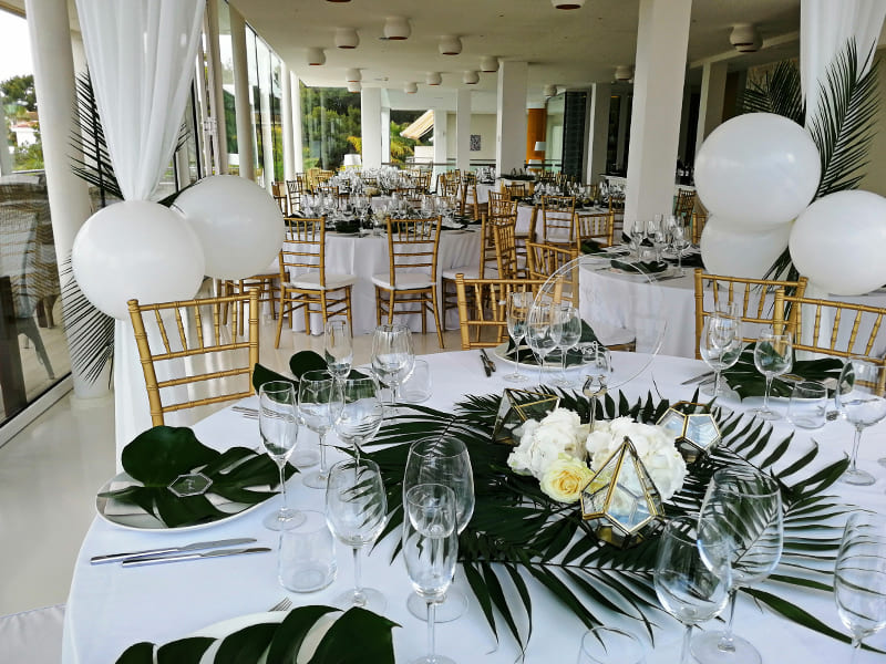 Sala de boda con mesas decoradas con oro y hojas de palmera