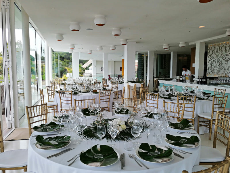 Comedor con mesas redondas y decoradas con hojas de palmera y ramos de flores
