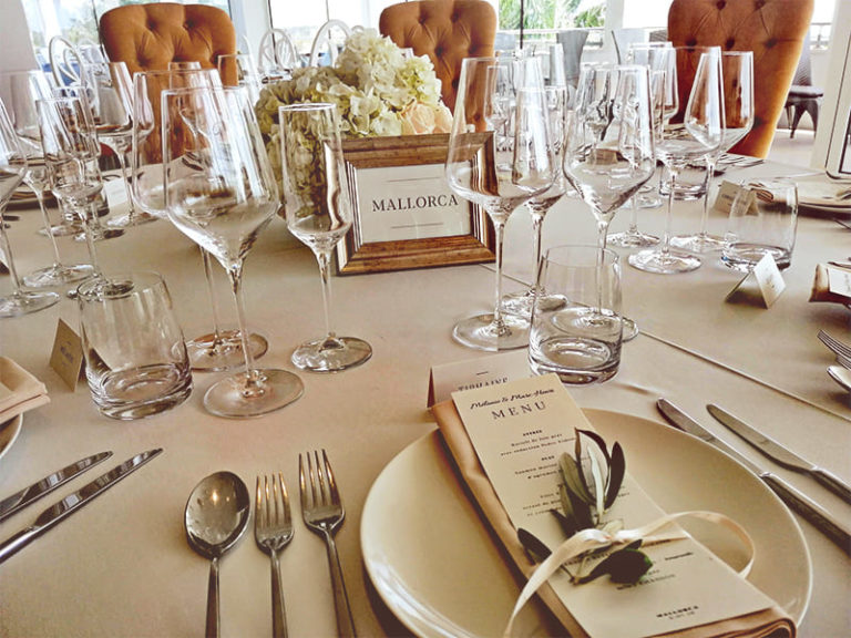 Una mesa decorada con muchos cubiertos, vasos de vino y un ramo de flores