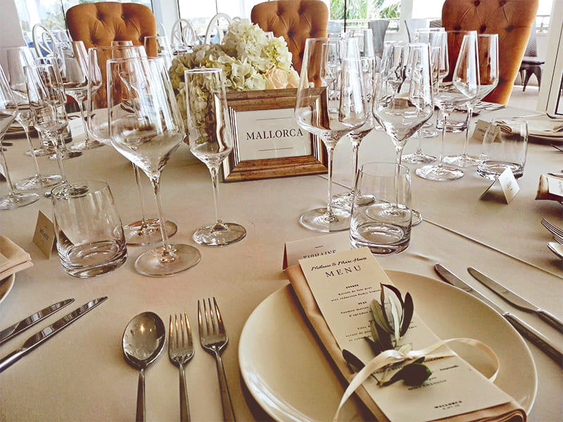 Una mesa decorada con muchos cubiertos, vasos de vino y un ramo de flores